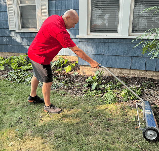 lp-Nail-Rolling an employee in a red shirt using a magnetic roller to collect any nails in the grass